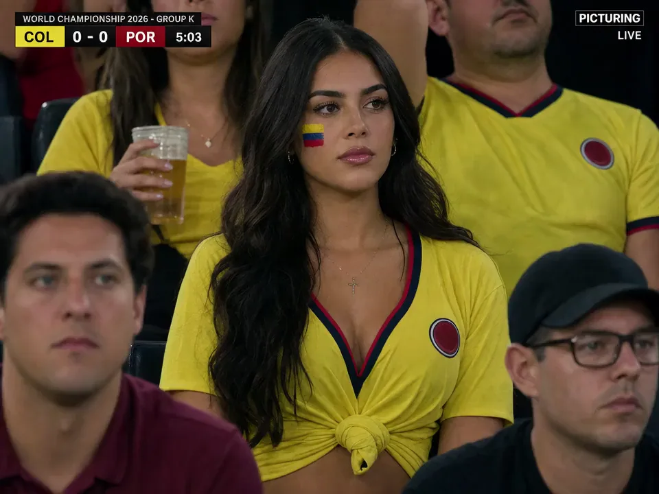 A supporter in a stadium crowd during a televised match, broadcast graphics across the frame